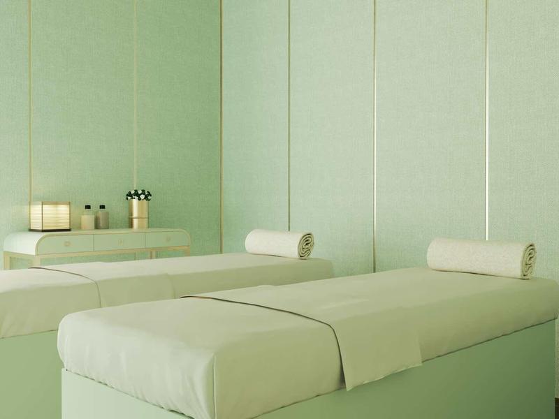 Zwei weiße Massageliegen mit kleinen Rollenpolstern in einem hellgrünen, minimalistischen Raum.