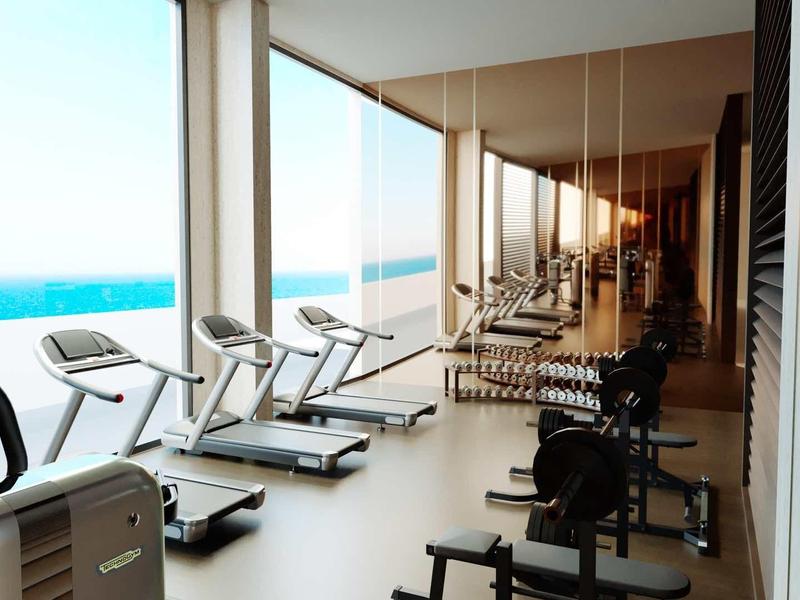 Fitnessraum mit Laufbändern und Kraftgeräten, große Fenster mit Blick auf das Meer und helles Tageslicht.