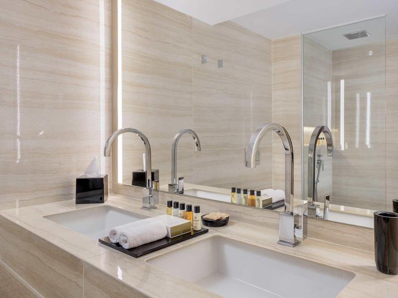 Moderner Badezimmerwaschtisch aus hellem Marmor mit zwei Becken, Spiegel und LED-Lichtbändern.