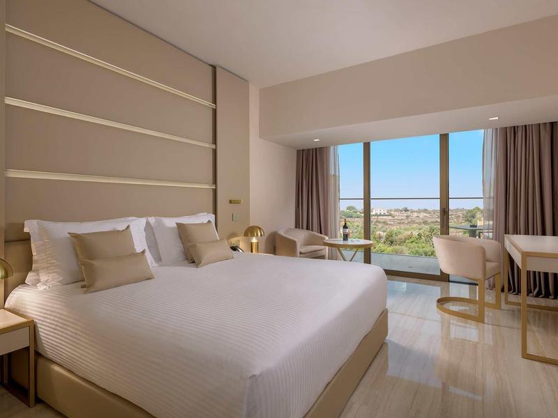 Modernes Hotelzimmer mit großem Bett, beigem Farbschema und Panoramafenster mit Aussicht.