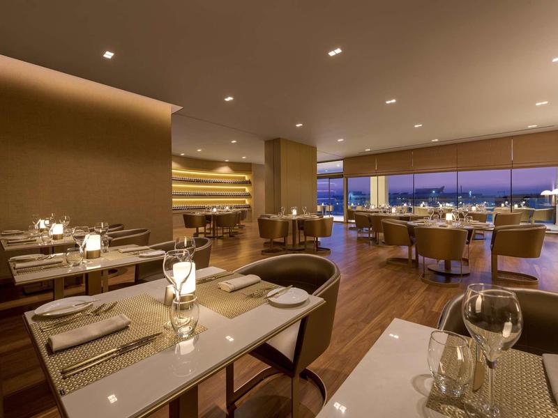 Modernes Restaurant mit Holzboden, gedeckten Tischen und großer Fensterfront bei Dämmerung.