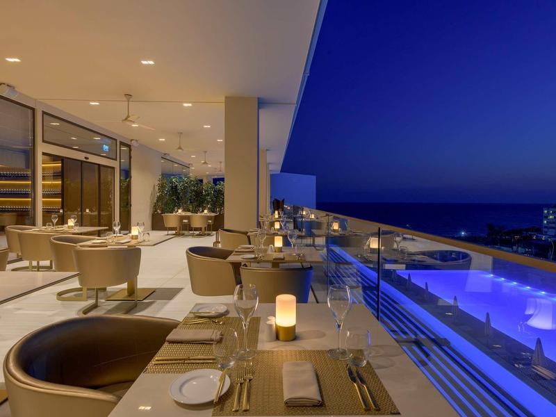 Moderne Terrasse mit runden Sesseln, gedeckten Tischen und beleuchtetem Pool bei Nacht.