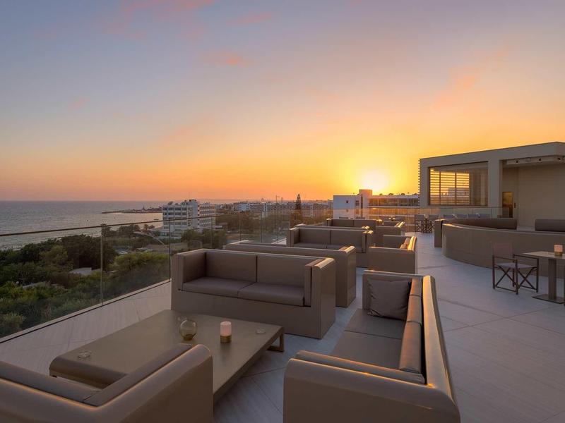Dachterrasse mit modernen Sitzmöbeln, Blick auf Sonnenuntergang und Meer am Horizont.