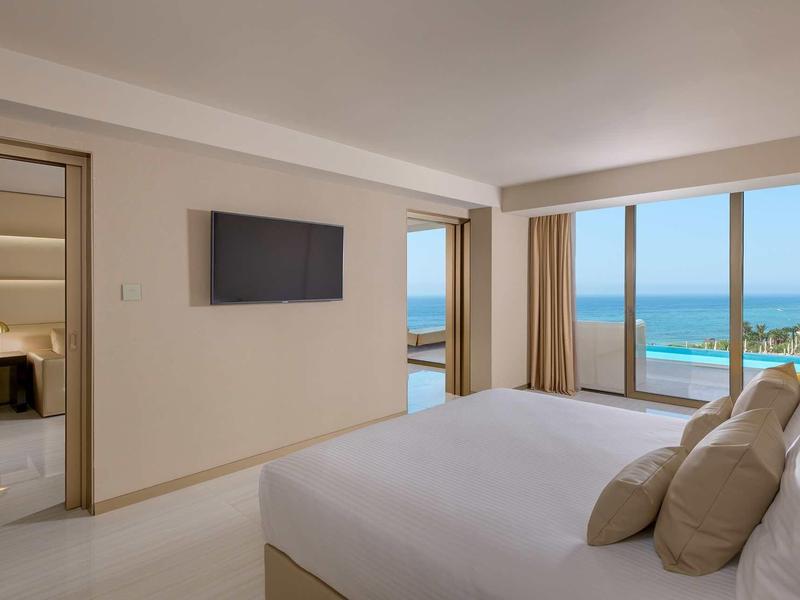 Modernes Schlafzimmer mit großem Bett, Flachbildfernseher und Meerblick durch Fenster.