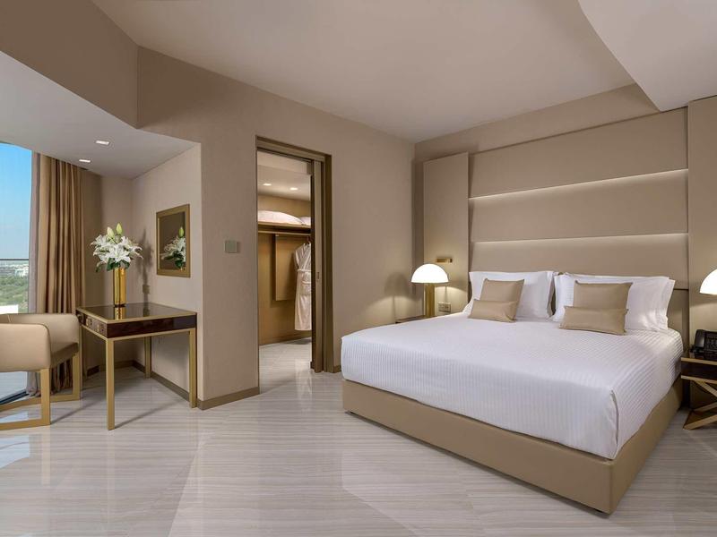 Modernes Schlafzimmer mit großem Bett, zwei Nachttischen, Stuhl, Schreibtisch und großem Fenster.