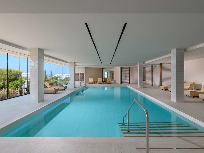 Moderner Innenpool mit großen Fenstern, weißen Wänden und gemütlichen Sitzbereichen in hellem Raum.