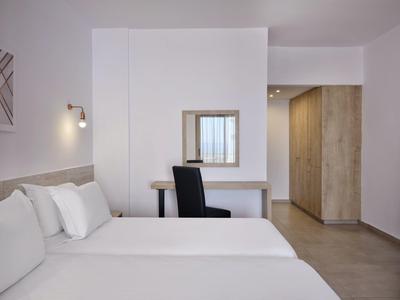 Schlichtes, modernes Schlafzimmer mit weißem Bett, schwarzem Stuhl und Holzmöbeln.