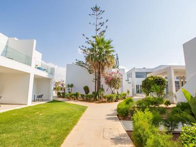 Wohnanlage mit weißen Gebäuden, gepflegtem Garten, Palmen und Gehweg unter blauem Himmel.