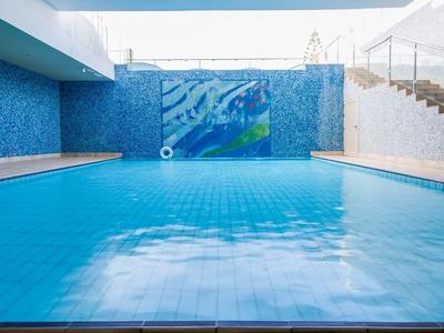 Großes Schwimmbecken mit klar blauem Wasser, Mosaikfliesen und Treppen rechts zum Beckenrand.