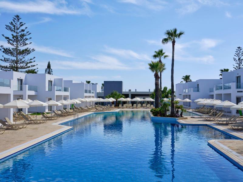 Moderner Außenpool mit blauen Wasser, weißen Liegestühlen und Palmen unter blauem Himmel.