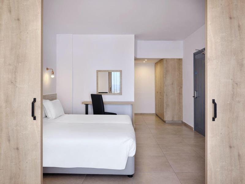 Modernes Hotelzimmer mit großem Bett, Schreibtisch, Stuhl und sanfter Beleuchtung.