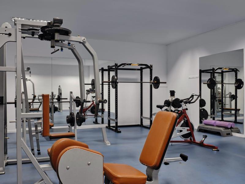 Moderne Fitnessräume mit verschiedenen Trainingsgeräten, Spiegeln und blauem Bodenbelag.