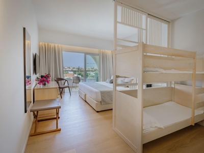 Chambre d'hôtel avec lits superposés, lit double et balcon avec vue sur la montagne.