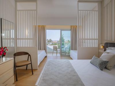 Chambre d'hôtel lumineuse avec deux lits simples, lit double, balcon et vue sur la mer.