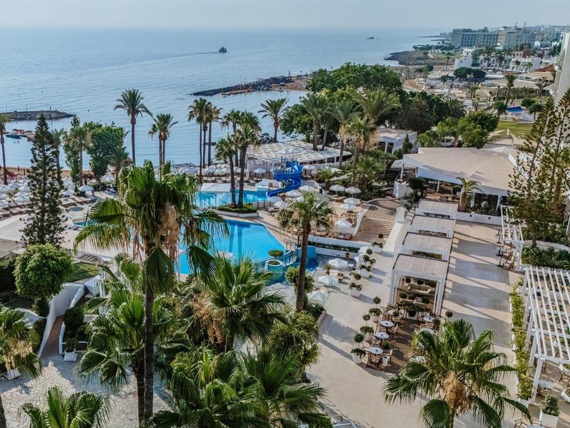 Piscine d'hôtel avec chaises longues, palmiers et vue sur la mer à la plage.