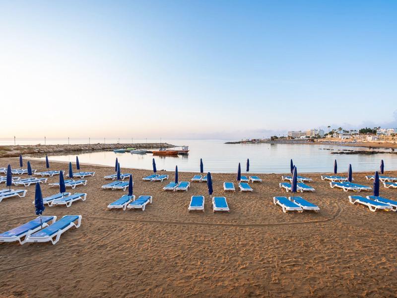 Chaises longues vides et parasols fermés sur la plage de sable calme sous un ciel clair.
