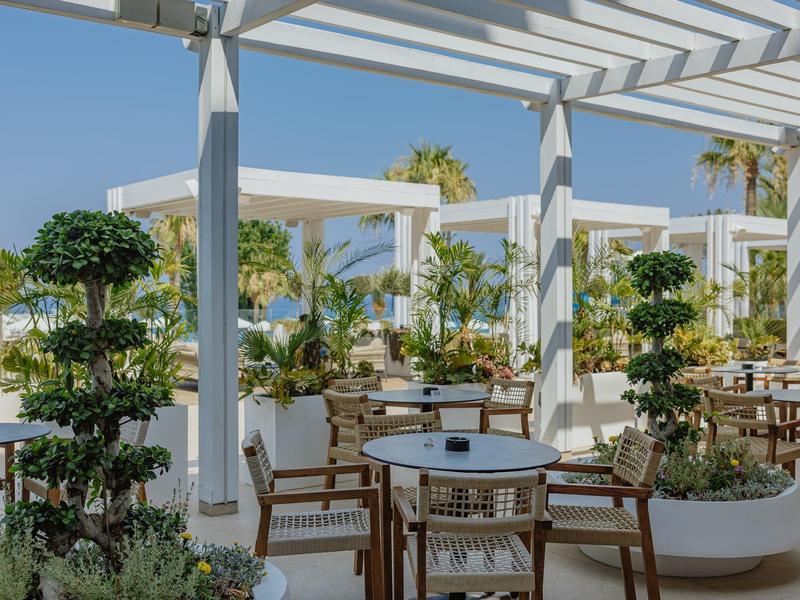 Terrasse ensoleillée avec des pergolas blanches, tables et chaises dans un cadre tropical.
