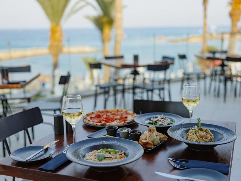 Table avec plats italiens et boissons sur terrasse avec vue sur la mer au coucher du soleil