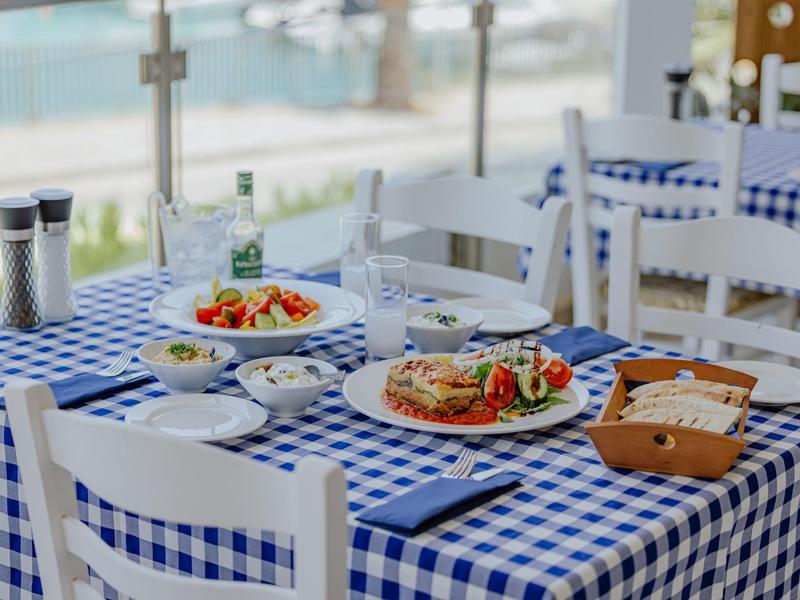 Table avec nappe à carreaux bleus et blancs, servie avec des plats méditerranéens et vue sur l'eau.