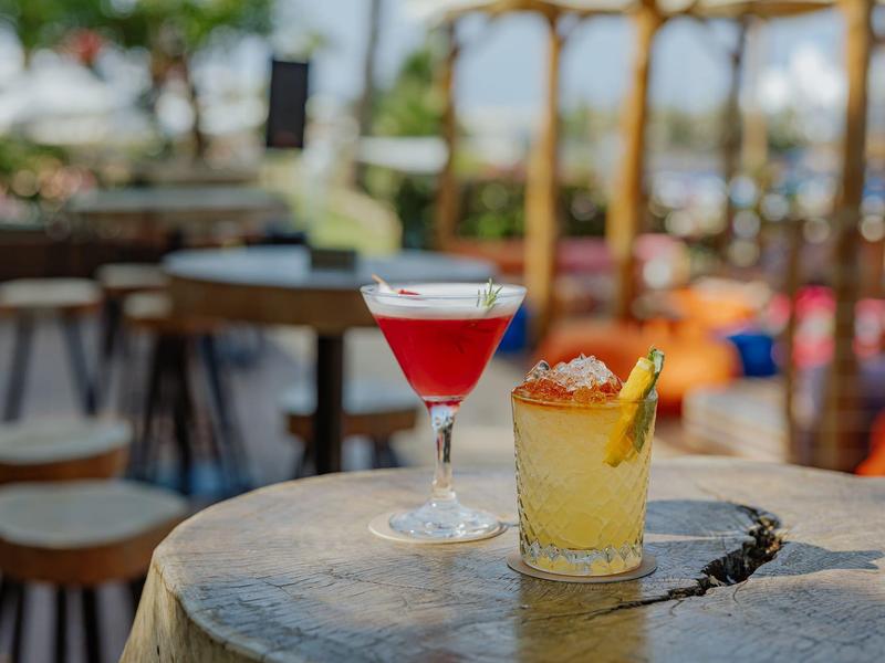 Deux cocktails colorés posés sur une table rustique dans un bar en plein air.