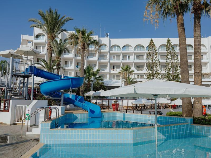 Hôtel avec piscine extérieure, toboggan aquatique et palmiers sous un ciel bleu clair.