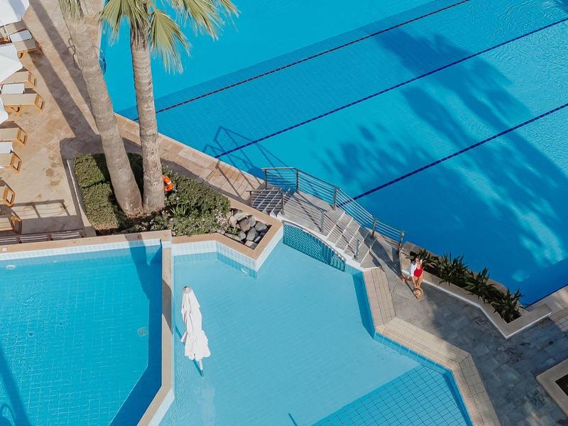 Vue aérienne d'une piscine d'hôtel bleue avec chaises longues et palmiers.