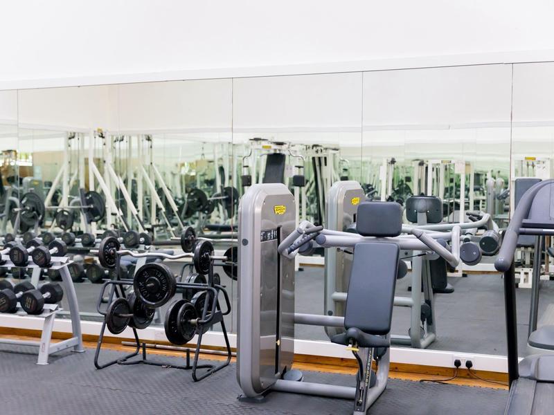 Salle de sport moderne avec poids, appareils d'exercice et grands miroirs au mur.