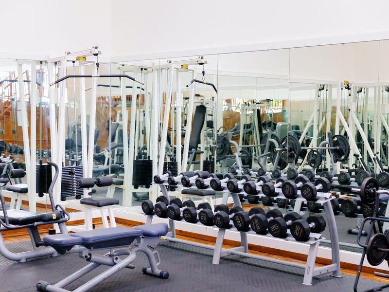 Salle de sport moderne avec haltères, équipements d'entraînement et miroirs muraux.