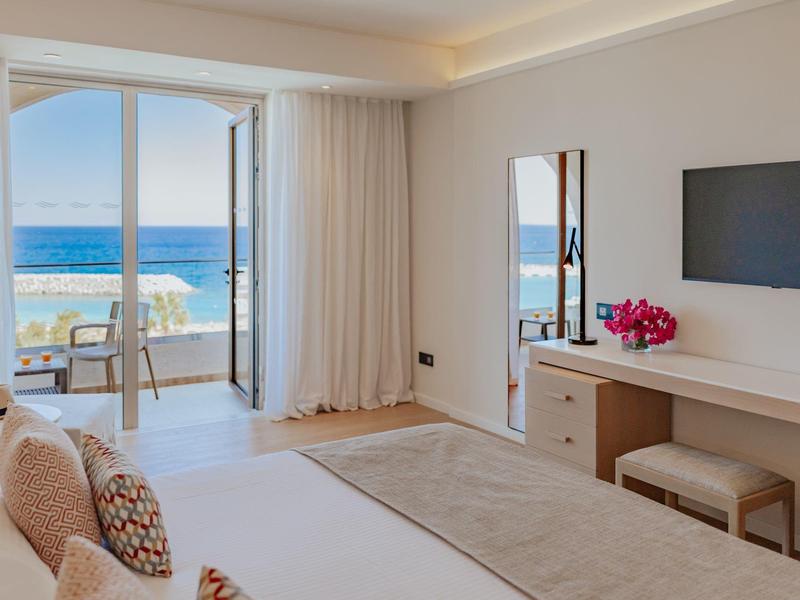 Chambre d'hôtel moderne avec vue sur la mer, décoration blanche et balcon avec chaise.