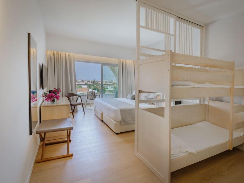 Chambre d'hôtel avec lits superposés, lit double et balcon avec vue sur la montagne.