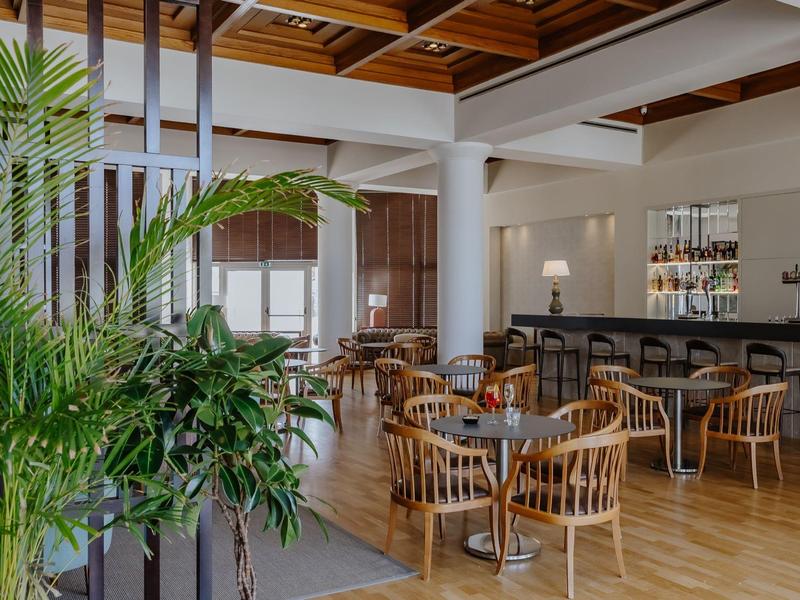 Intérieur moderne de bar d'hôtel avec plafond en bois, chaises en bois et plantes vertes.