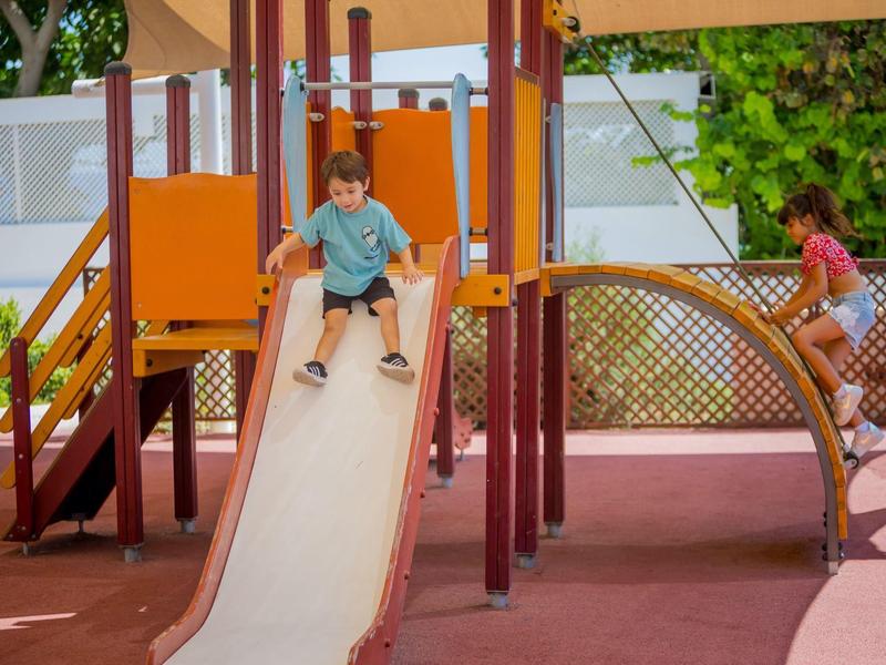 Deux enfants jouent sur un toboggan orange dans une aire de jeux.