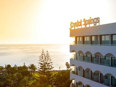 Bâtiment de l'hôtel avec balcons, arbres et mer au coucher du soleil.