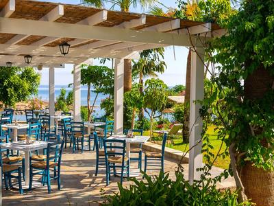Offener Außenbereich eines Restaurants mit blauen Stühlen und Tischen unter Pergola mit Blick aufs Meer.
