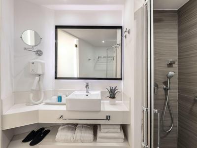 Salle de bain moderne avec lavabo, miroir, sèche-cheveux et cabine de douche dans une chambre d'hôtel.