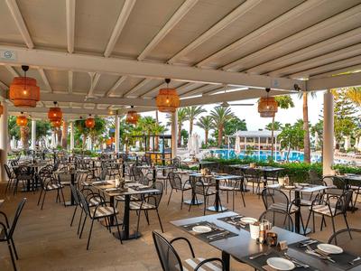 Restaurant ouvert avec tables dressées et vue sur la piscine et les palmiers.
