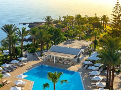 Hotelresort mit großem Pool, Liegestühlen und Blick auf das Meer bei Sonnenuntergang.