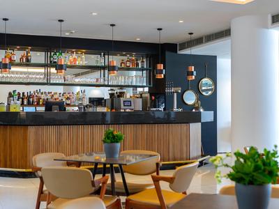 Moderne Hotelbar mit Holztheke, stilvollen Sitzgelegenheiten und Pflanzen als Dekoration.