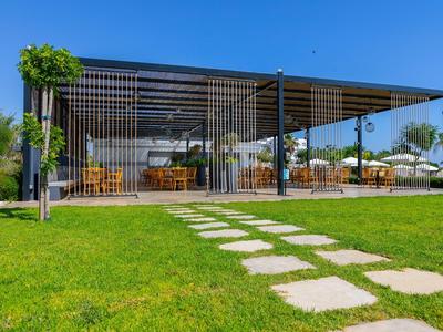 Modernes Restaurant mit Außensitzbereich und Weg aus Steinplatten auf grünem Rasen.
