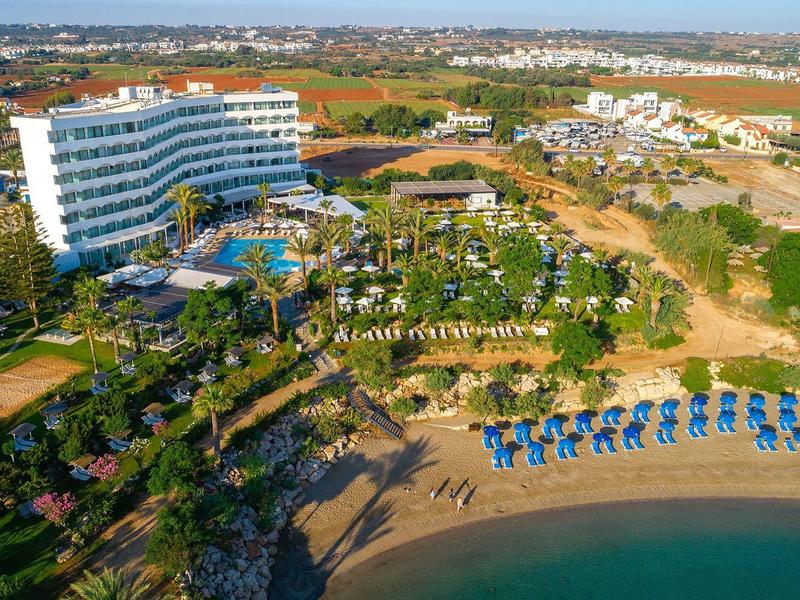 Vue sur un grand hôtel avec piscine, plage et parasols au bord de la mer.