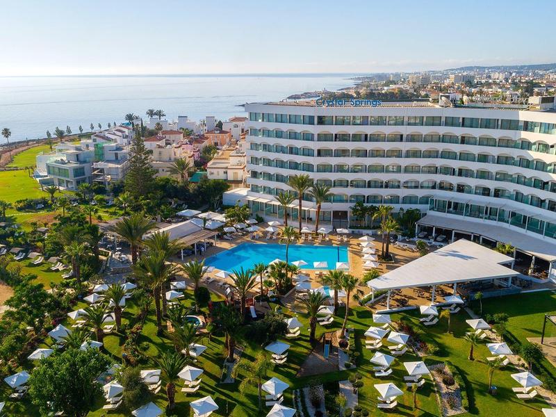 Hôtel avec grande piscine, jardin environnant et vue sur la mer dans une station balnéaire ensoleillée.