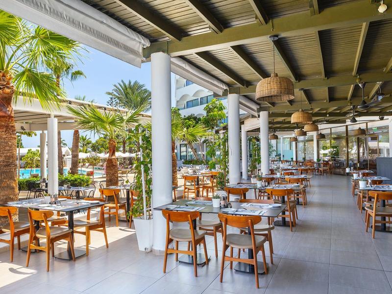 Grand restaurant ouvert avec de nombreuses tables en bois et des plantes tropicales.