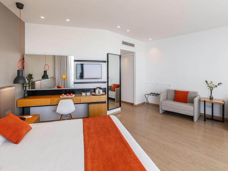 Chambre d'hôtel moderne avec lit double, bureau et coin salon aux tons clairs.