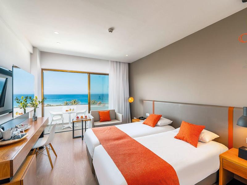Chambre d'hôtel moderne avec lit double, vue sur la mer et décoration orange.