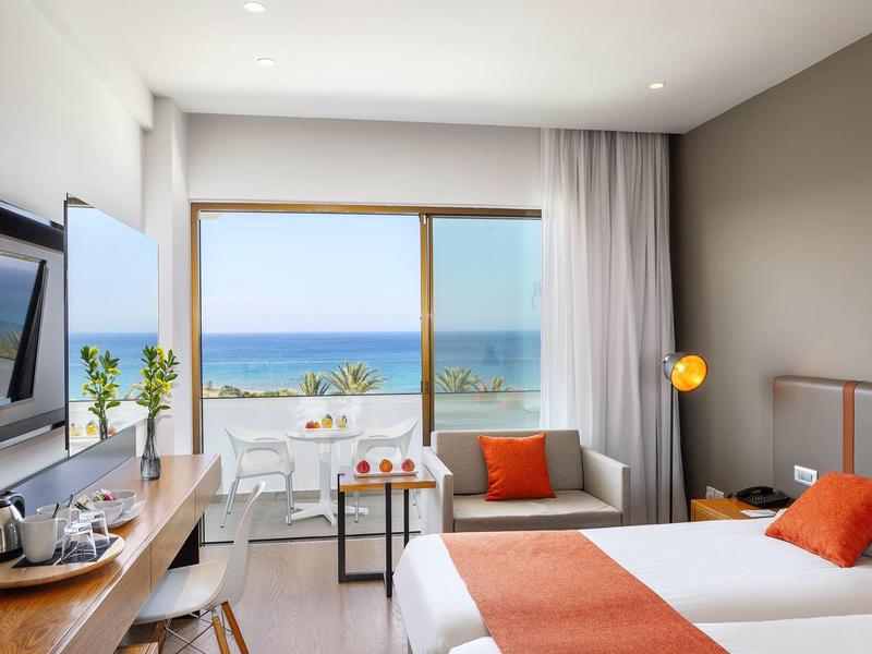 Chambre d'hôtel moderne avec vue sur la mer, lit double et intérieur élégant aux tons chauds.