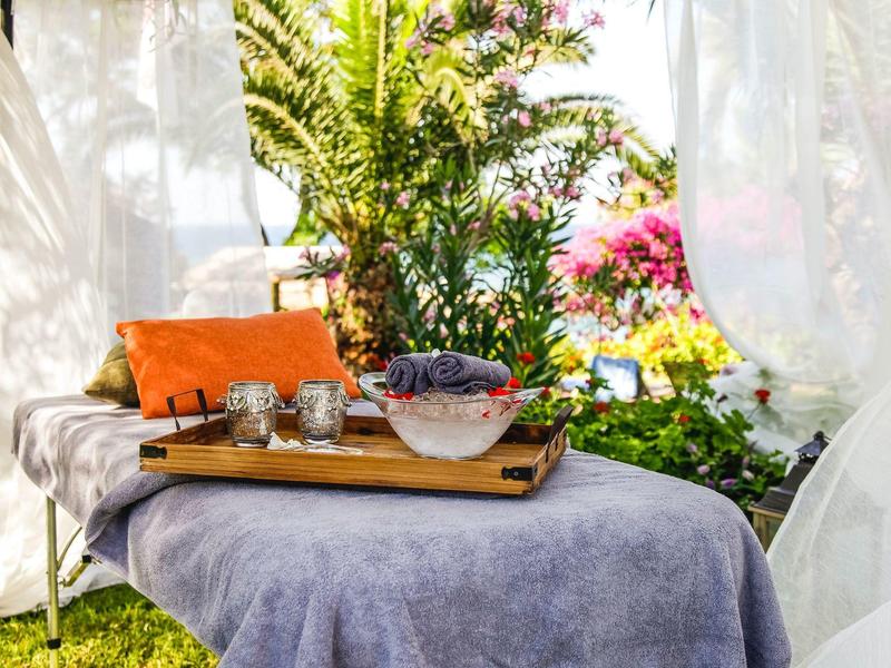 Banc de massage confortable avec serviette et coussin dans un jardin avec rideaux blancs.