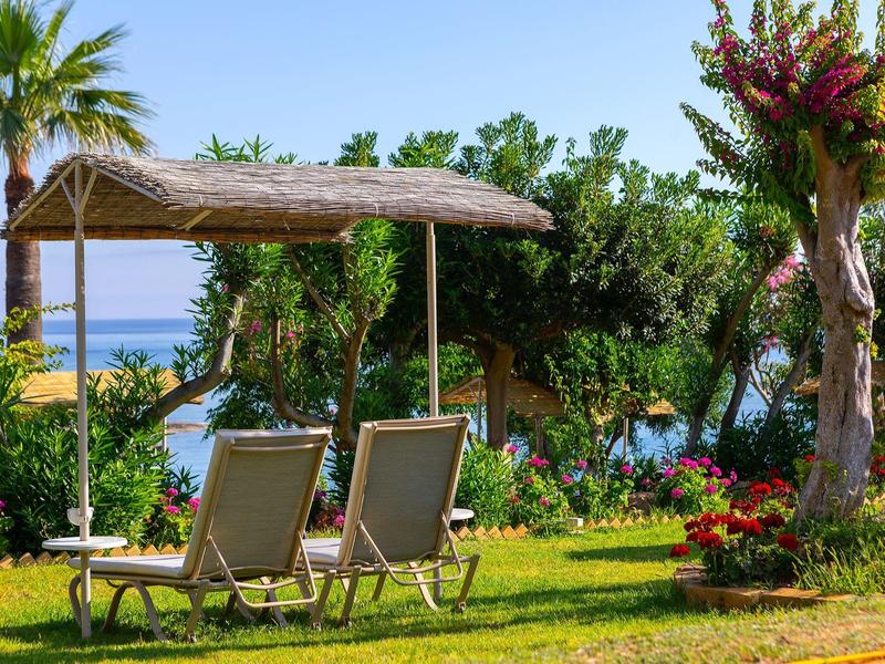 Deux chaises longues sous un toit de chaume avec vue sur la mer dans un jardin tropical