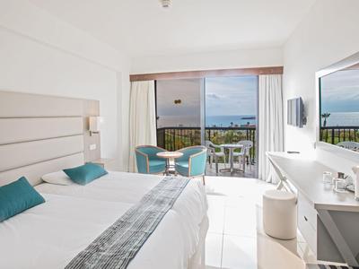 Habitación de hotel luminosa con cama doble, zona de estar y balcón con vista al mar.