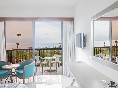 Moderner Hotelzimmerbereich mit Blick auf Balkon und Meer im Hintergrund bei Sonnenuntergang.