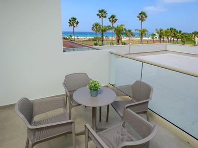 Balkon mit grauen Stühlen und runder Tisch, Blick auf Palmen und Meer im Hintergrund.